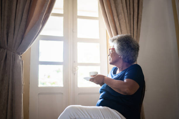 istock Contemplative senior woman looking through the window while drinking coffee at home 1368004786