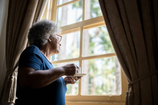 istock Contemplative senior woman looking through the window while drinking coffee at home 1368004821