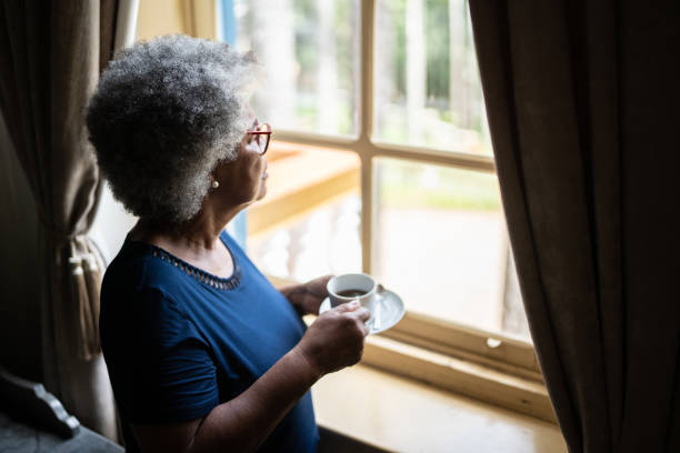 istock Contemplative senior woman looking through the window while drinking coffee at home 1368004824