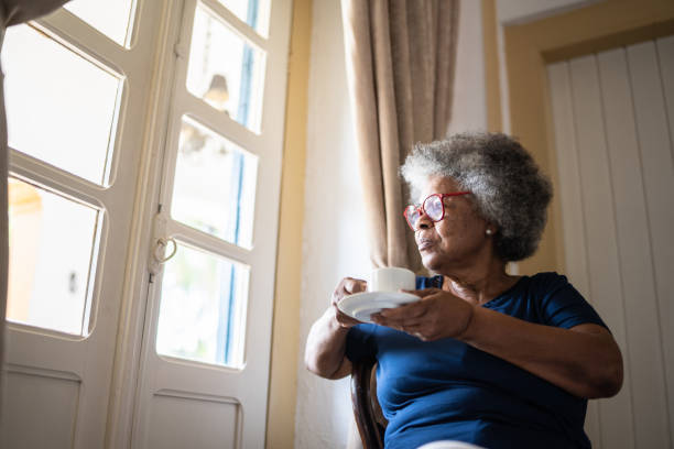 istock Contemplative senior woman looking through the window while drinking coffee at home 1368004836
