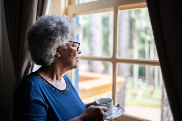 istock Contemplative senior woman looking through the window while drinking coffee at home 1368004845