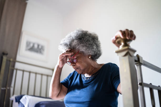 donna anziana con mal di testa seduta nel letto di casa - senior male foto e immagini stock