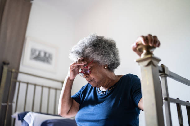 senior woman with headache sitting in the bed at home - hastalık belirtisi fotoğraflar stok fotoğraflar ve resimler