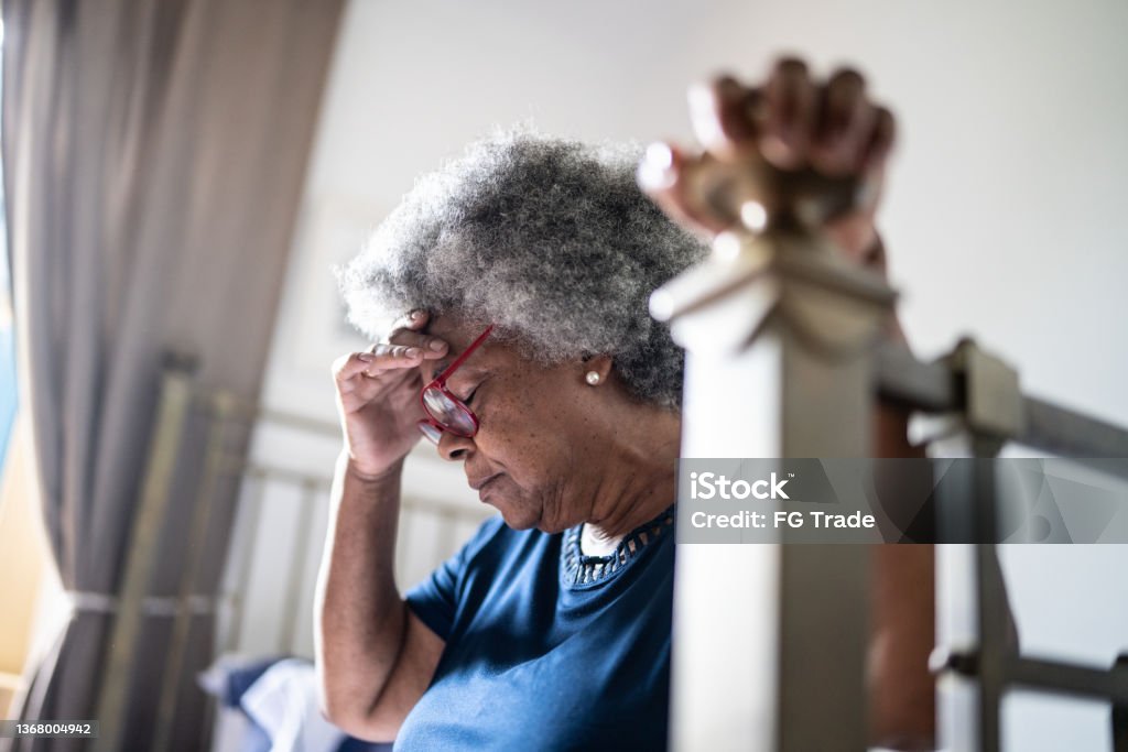 Senior woman with headache sitting in the bed at home Heat - Temperature Stock Photo