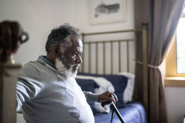 созерцательный пожилой мужчина сидит дома в кровати - tired men african descent sadness стоковые фото и изображения