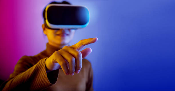 Asian woman wearing VR glasses pointing finger to do activities in the virtual world. Asian woman wearing VR glasses pointing finger to do activities in the virtual world on blue and purple background. virtual reality point of view photos stock pictures, royalty-free photos & images