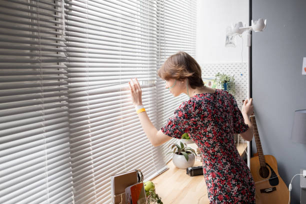 istock Sick young woman looking through venetian blinds 1368005966