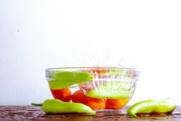 Some capsicum and tomatoes are falling in a bowl of water with a splash isolated on white background.