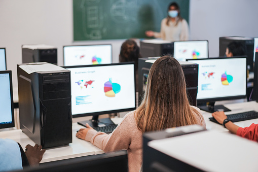 Multiracial students using computers during business class wearing safety masks at school - Focus on center girl head