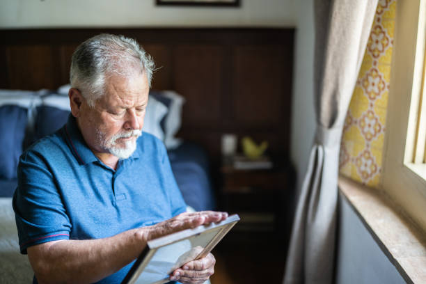 Senior man holding a picture frame missing someone at home