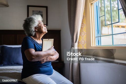 istock Senior woman holding a picture frame missing someone at home 1368009967