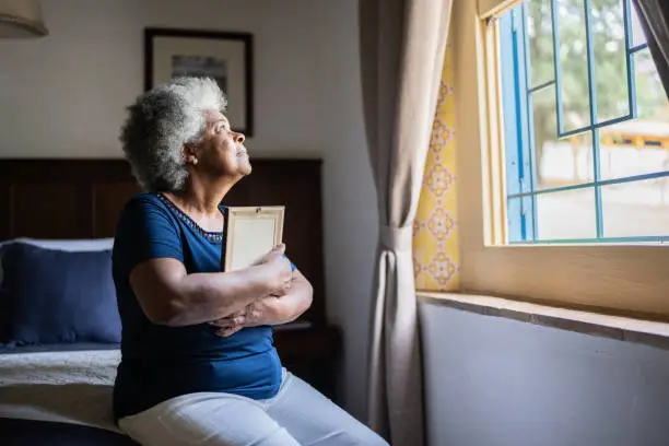 Photo of Senior woman holding a picture frame missing someone at home