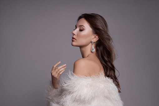 Beauty art portrait of a beautiful woman with long hair, white fur coat with long faux fur. Beautiful earrings in a woman's ears. Hairstyle, hair styling