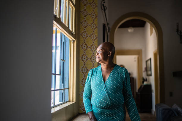 istock Senior woman looking through the window at home 1368011434