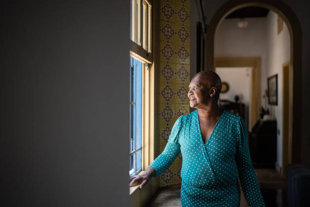 istock Senior woman looking through the window at home 1368011442