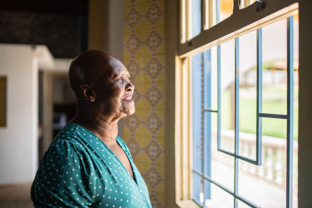 istock Senior woman looking through the window at home 1368011449