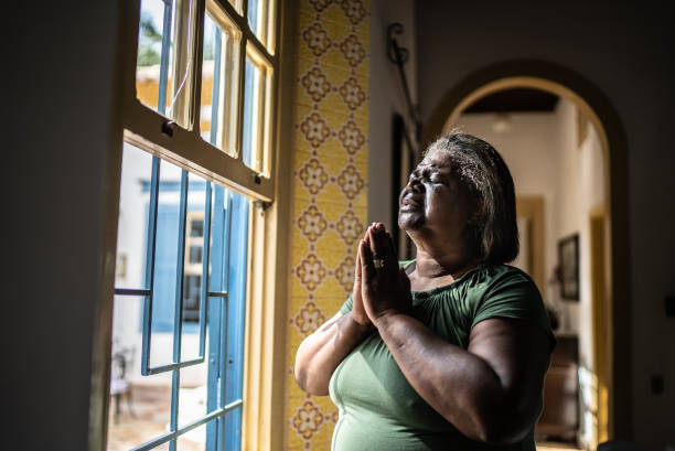 istock Senior woman praying at home 1368011469