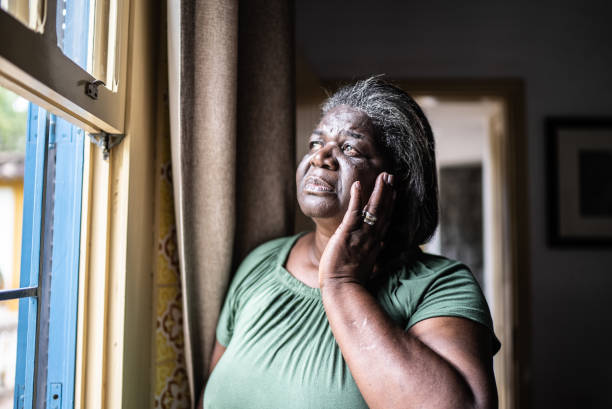 обеспокоенная пожилая женщина смотрит в окно дома - women sadness african ethnicity african descent стоковые фото и изображения