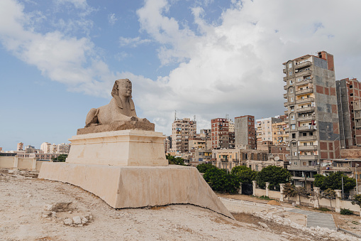 Statue of the ancient Sphinx on the background of modern houses and blue cloudy sky in Alexandria, Egypt