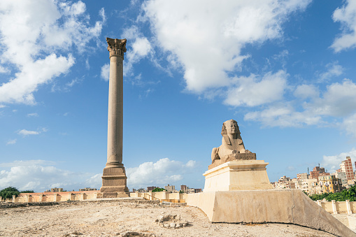 The famous Pompey pillar with a sphinx in the Upper Egyptian city of Alexandria. A popular travel destination. day and blue sky. A nice long exposure with moving clouds.