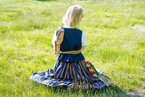 Latvian woman in traditional clothing posing on nature background in village. Retro vintage natural shoes leather bast shoes. Ligo festival.