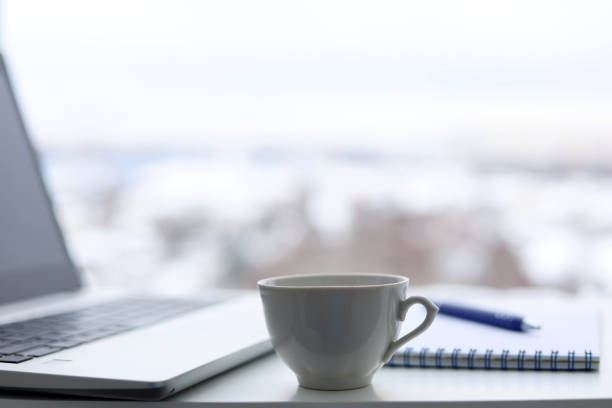 istock Tea cup, laptop and notepad with pen on a table against the window, view to winter city 1368013368