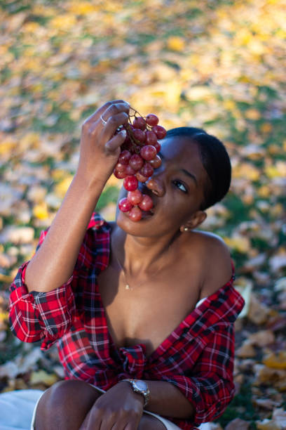Front view of a beautiful African lady eating grapes in a park.