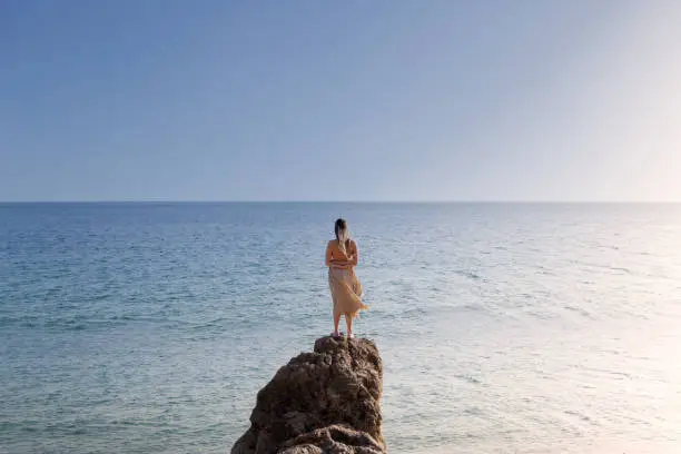 Woman photographed from behind wearing a flowing dress, appreciating the coastline scenario