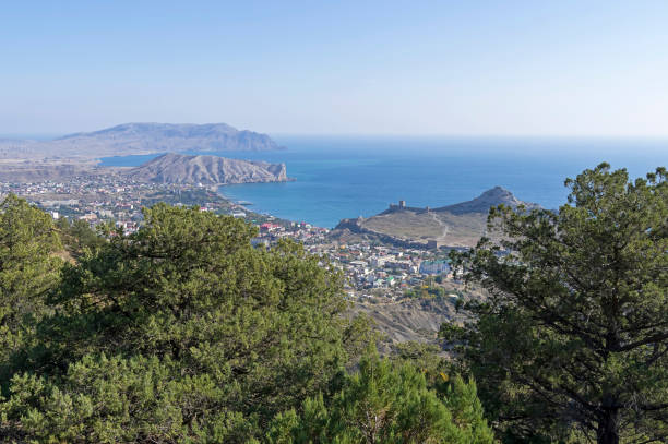View of the small resort town from the slope of the mountain. Crimea View of the resort town of Sudak from the mountain slope. Crimea, sunny day in October. juniperus excelsa stock pictures, royalty-free photos & images