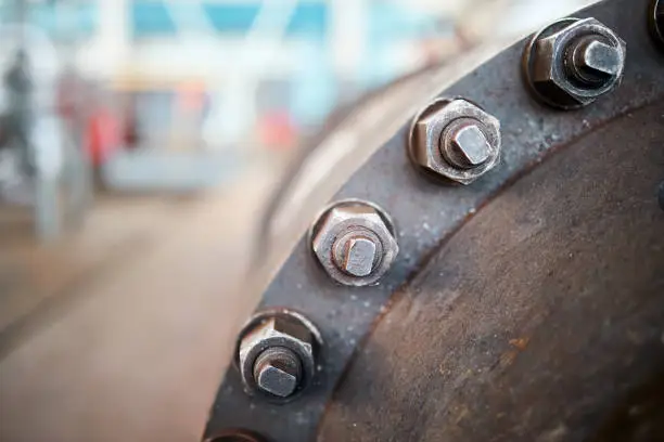 Photo of Industry flanges joint connection with screws and bolts closeup over out of focus abstract industrial background with copyspace. Bolted screw connection, sealing connection on manhole chemical plant.