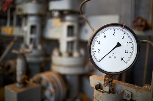 Pressure gauge or manometer shows zero closeup with crane or valve cover out of focus background, with copyspace. Example of chemical plant retro style equipment.