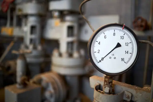 Photo of Pressure gauge or manometer shows zero closeup with crane or valve cover out of focus background with copyspace. Example of chemical plant retro style equipment.