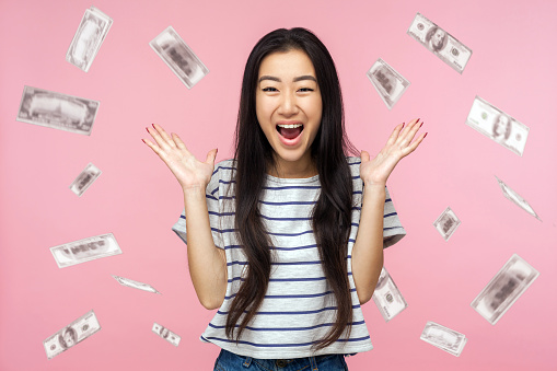 Oh my god, wow. Portrait of amazed young woman looking at camera with big eyes, absolutely shocked of money rain falling from up. indoor isolated on pink background
