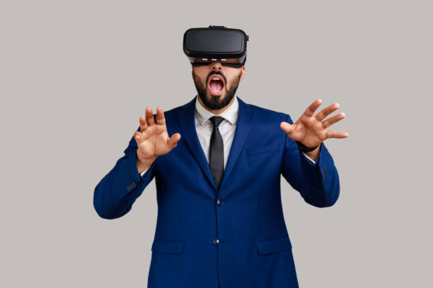 istock Man in vr headset, playing virtual reality game with shocked facial expression, outstretching hands. 1368018485