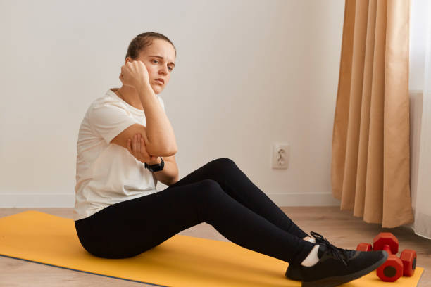 Indoor shot of sportswoman touching painful hand, sitting on mat, suffering joint injury after yoga, sport trauma elbow dislocation, muscle strain, inflamed ulnar nerve. foto en interiores de una deportista tocando una mano dolorosa, sentada en una colchoneta, sufriendo lesiones en las articulaciones después del yoga, traumatismo deportivo, dislocación del codo, distensión muscular, nervio cubital inflamado.