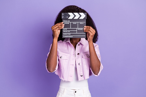 Photo of young african woman cover close face with movie film clapper wear lilac jacket isolated on violet color background.
