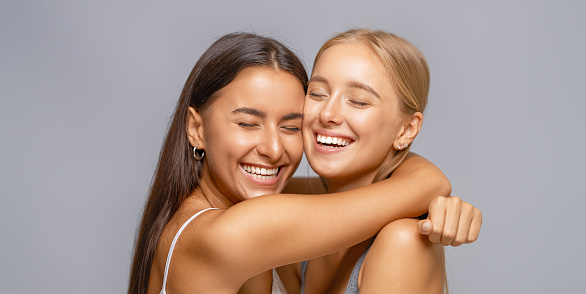 Portrait of two cheerful young women standing together and hugging.