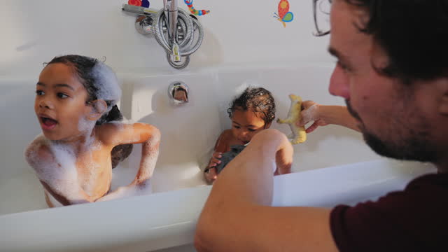 Parents giving toddler daughters a bath, playing with toys in bathtub