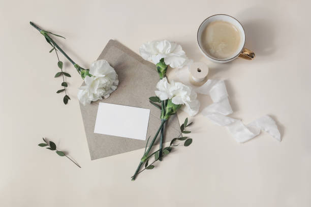 istock Breakfast still life. Greeting card, invitation mockup with envelope. Wedding, birthday stationery. Cup of coffee, white carnation flowers and eucalyptus branches. Beige table background. Flat lay. 1368030614