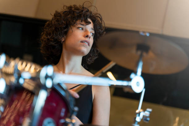 Portrait of a young woman with curly hair playing the drums in a recording studio Portrait of a young woman with curly hair playing the drums in a recording studio and looking to the window. drummer stock pictures, royalty-free photos & images