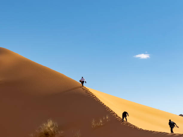 istock Unrecognizable tourists climbing with difficulty along the crest of a high sand dune. 1368035818