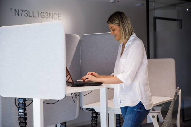 istock Smiling young businesswoman using standing desk, typing data on laptop 1368036810