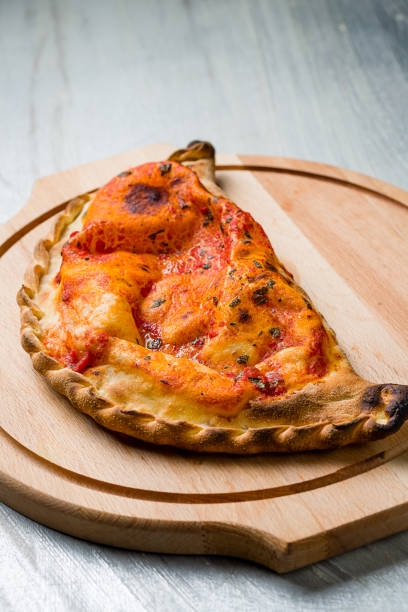 Closed calzone pizza with ham, cheese and tomato sauce on the board on grey table macro close up