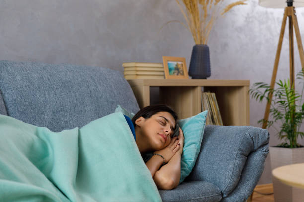 istock Young woman taking a nap on the cozy sofa under a warm blanket 1368037244