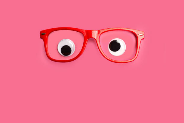 Googly eyes with red eyeglasses on a pink  background  with copy space