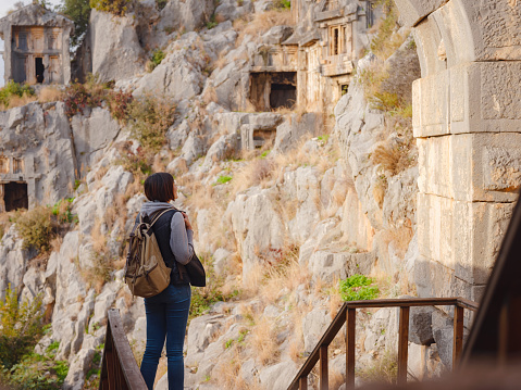 Archeological remains of the Lycian rock cut tombs in Myra, city Demre in Turkey. unique ancient necropolis. Woman tourist on ruins of ancient city exploring architecture