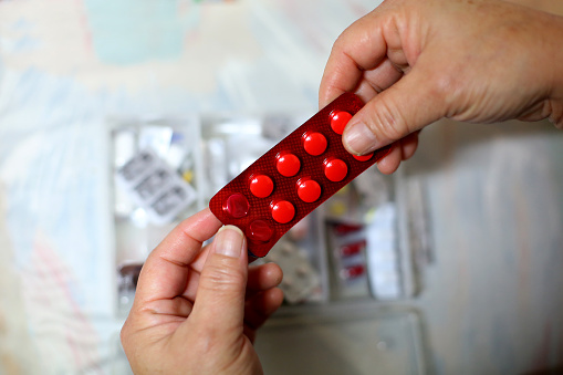 An Asian woman is holding strip of medical pills.