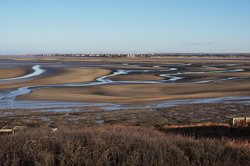 Hilbre Island. Wirral, England - 13 January 2022: Looking down on the Dee Estuary close to low tide. A large area of mudflat / sand flat is exposed, with a number of streams draining the seawater. The town of Hoylake can be seen on the far shoreline.