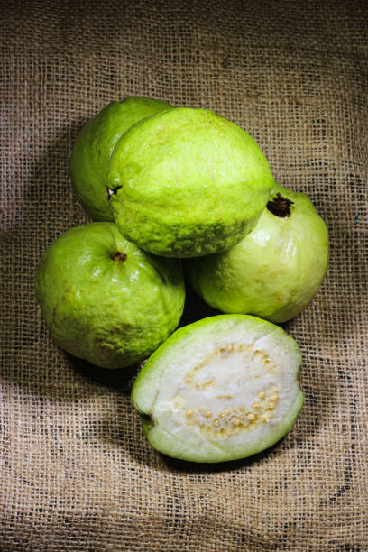 haufen grüner guave und ihre scheibe auf einem jute-texturhintergrund. guavenfrüchte aus der nähe. - guave stock-fotos und bilder