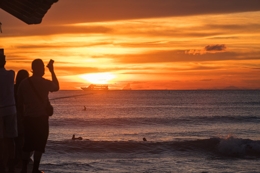 Oahu, USA - Oct 28, 2021: People watching a vivid sunset off the Waikiki Wall pier off the Queens Beach.
